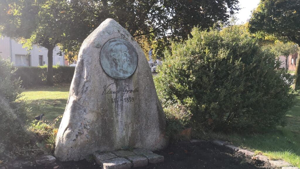 Das Foto zeigt den Klaus-Groth-Gedenkstein in Heide. Darauf zu sehen, ist ein Bildnis des Dichters, darunter stehen sein Name sowie Geburts- und Todesjahr (1819-1899).