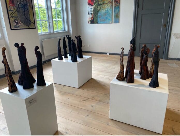 Eines der Ausstellungsstücke: drei weiße Würfel, auf denen je vier lange, schwarze Figuren stehen, die wie Menschen aussehen.