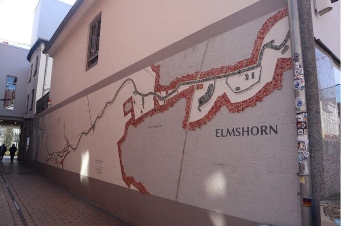 Ein Bild einer Hauswand auf der eine Malerei des Flusses Krückau dargestellt ist. Um die Krückau ist die Silhouette der Stadt von oben abstrakt dargestellt.